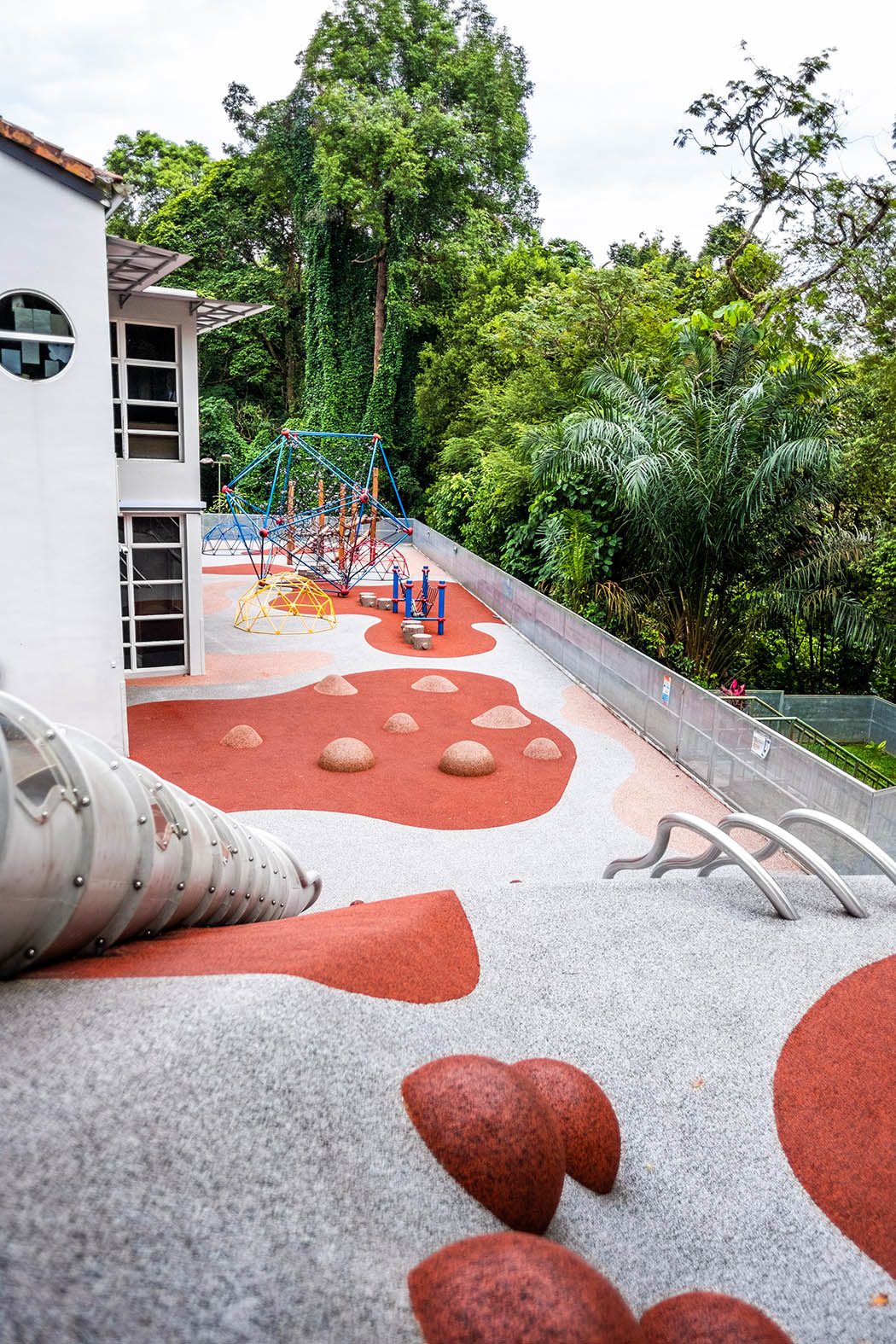 Playground landscape with a slide, climbing grips, knotted ropes, steel poles, and play mounds for active exploration.