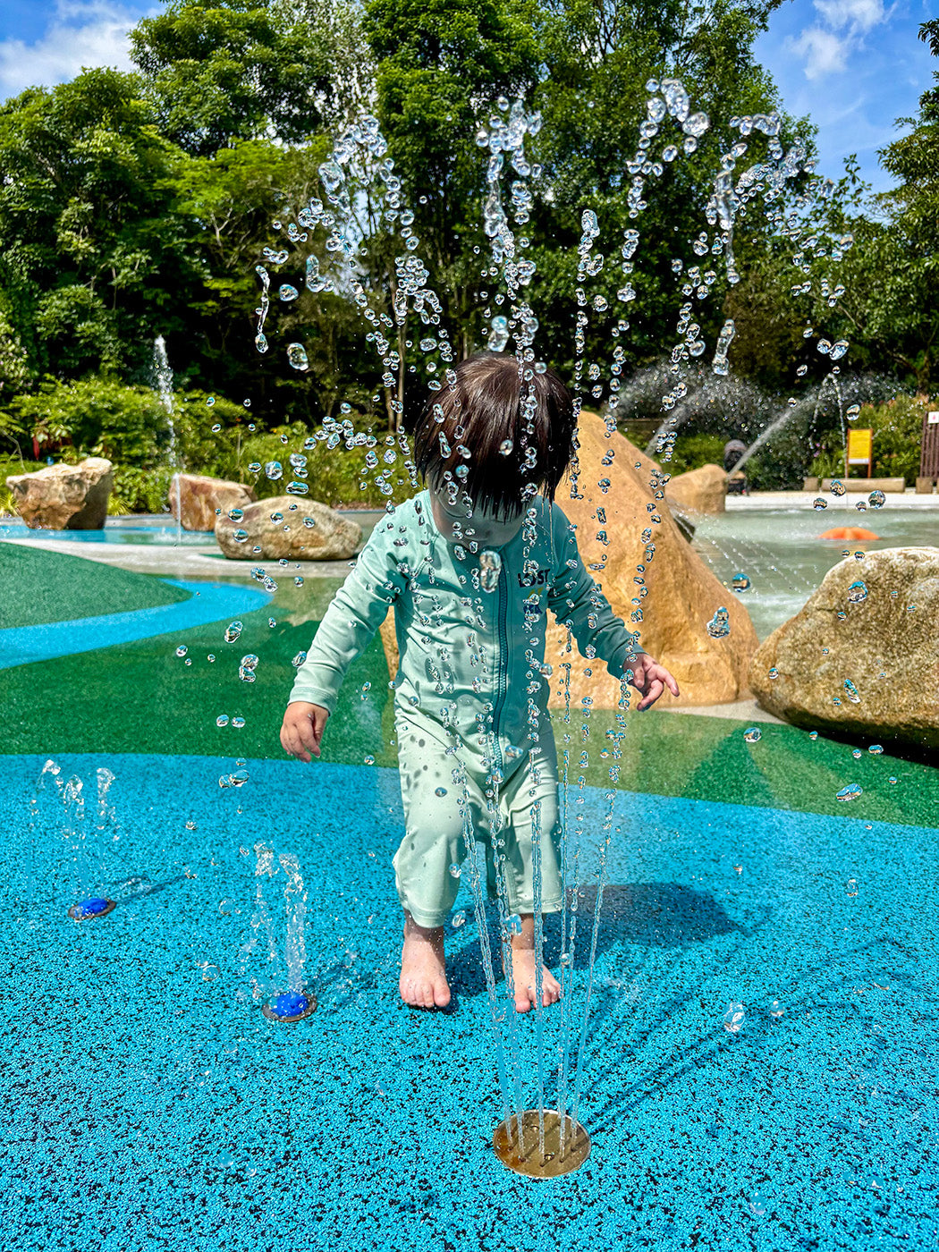 Child enjoying the gentle jets from the water play equipment at Jacob Ballas Children's Garden, promoting sensory play.