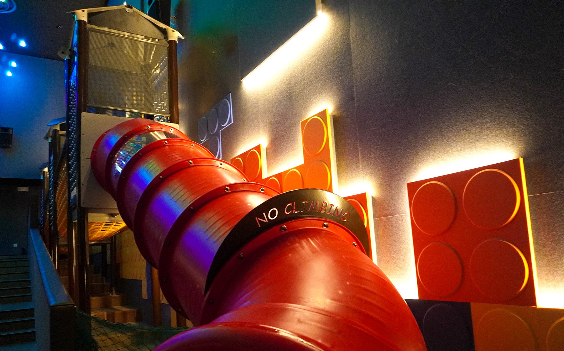 Bright red tube slide at Shaw Dreamers playground features a clear no-climbing sign, promoting safe and enjoyable play.