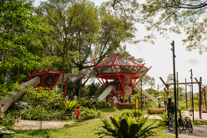 Children are playing happily on multiple slides and a rope tunnel while parents chat and watch them from nearby.