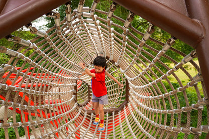 A boy passes through a rope tunnel, embarking on an adventurous journey with a look of excitement on his face.