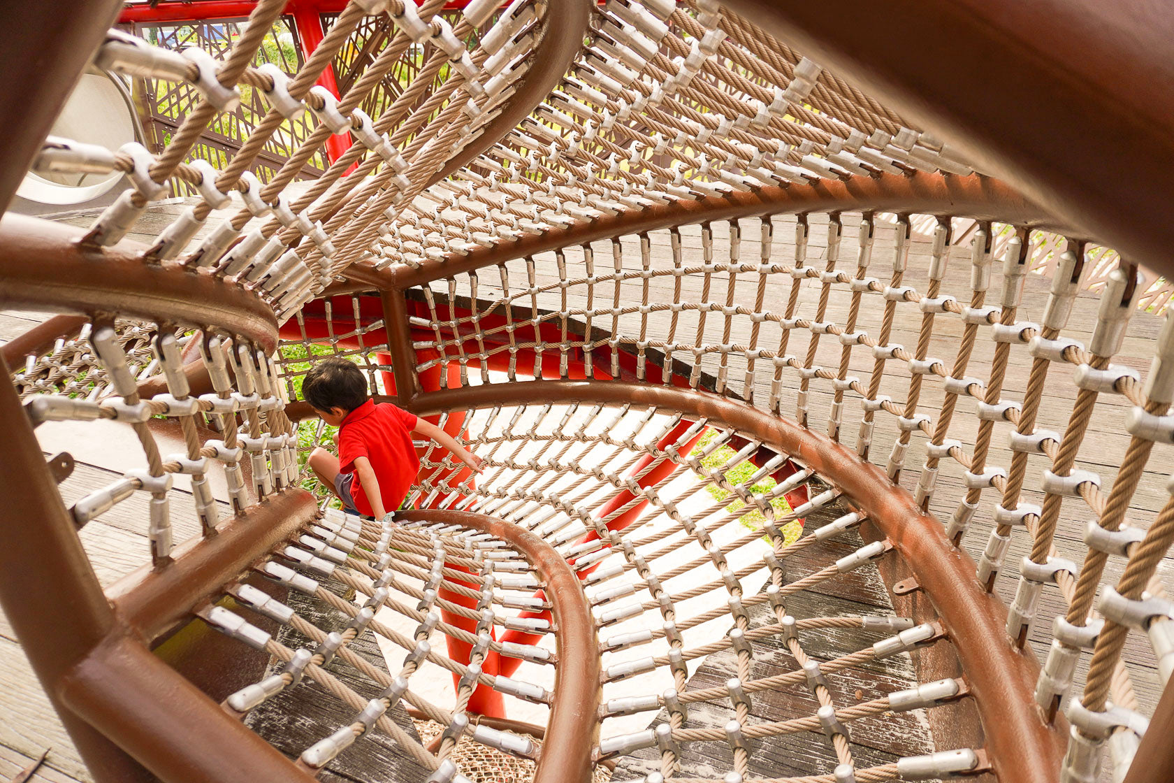 A boy slides through a rope tunnel, smiling with excitement as he plays.