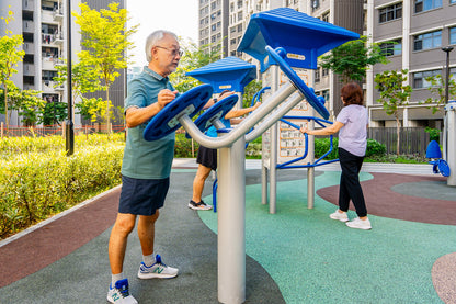 An elderly person exercises on an arm rotation machine, focusing on their workout in an outdoor gym 