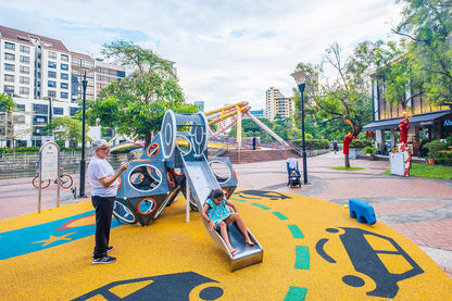 A girl slides down the Playworld PlayCube slide as a man captures the joyful moment in a photo.