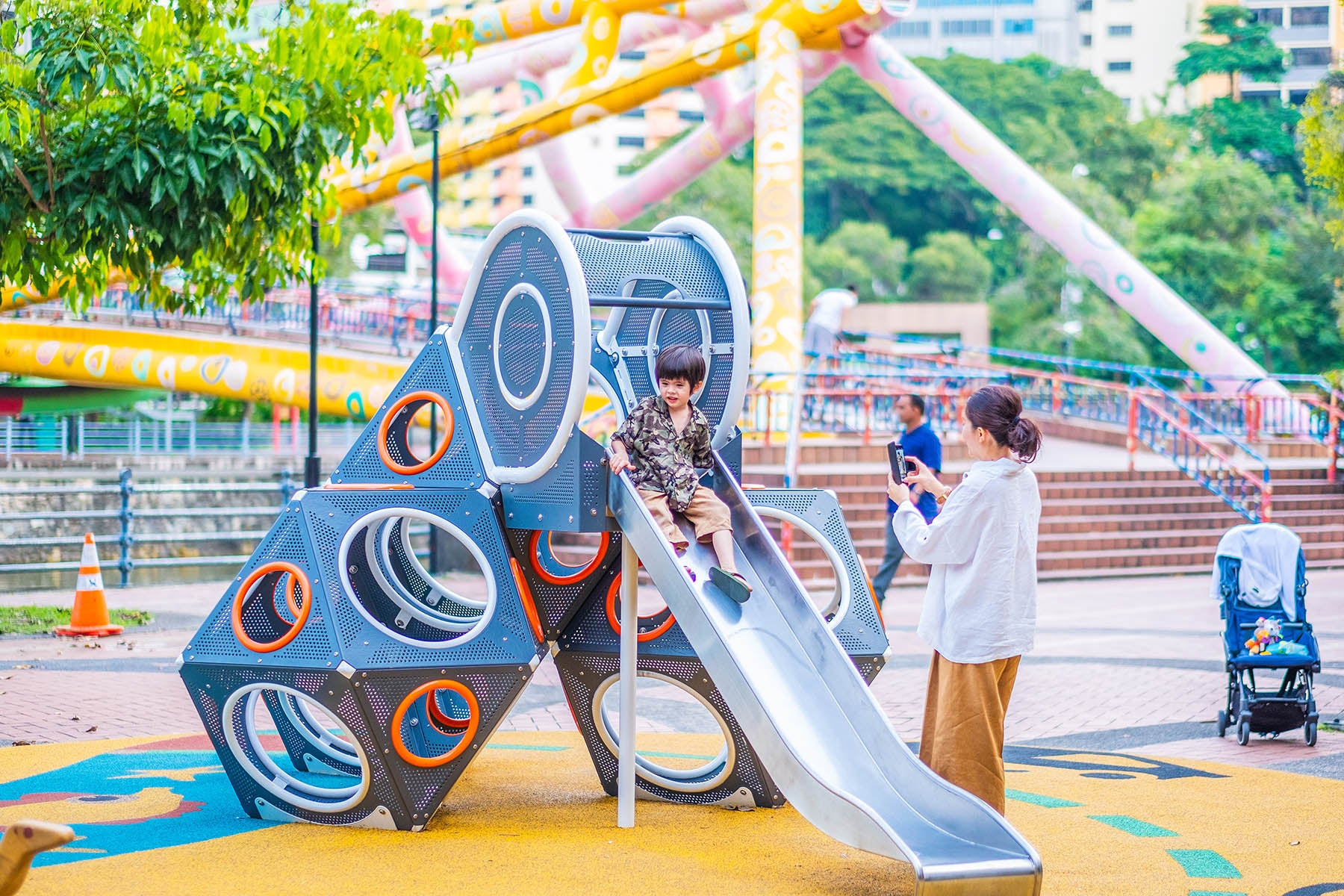 A boy slides down the Playworld PlayCube slide as his mom captures the joyful moment in a photo.