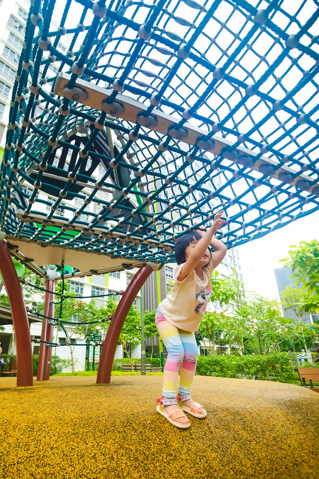 The girl attempts to traverse the Berliner playground net, carefully gripping the ropes as she enjoys the challenge.