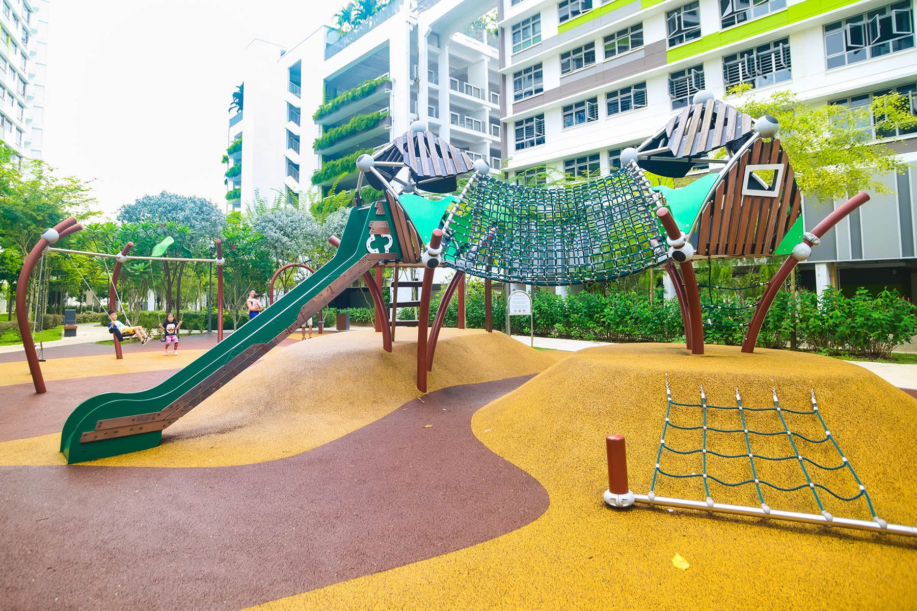 Berliner playground features a climbing net, swings, and a slide, offering various fun activities for children to explore.